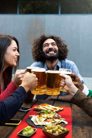 Happy and smiling caucasian man toasting with friends with beer in a bar outdoors. Celebratory toast. Vertical image.の写真素材
