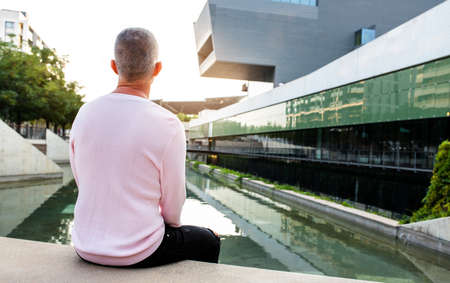 Caucasian man with pink sweater looking to a serene modern city view. Relaxing in the city. Copy space.の写真素材