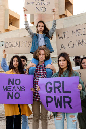 Young female protester sitting on mans shoulders holds a no means no signs in a demonstration....