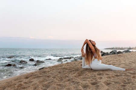 Young flexible caucasian woman practicing yoga on the beach at sunset. Copy space.の写真素材