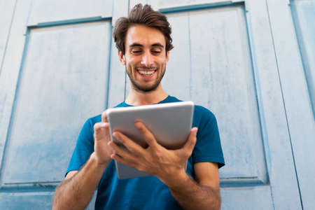 Happy smiling young caucasian man using digital tablet outdoors.の写真素材