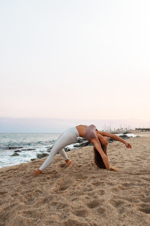 Young woman doing yoga at the beach. Female practices the wild thing yoga pose at sunset. Copy space. Vertical image.の写真素材