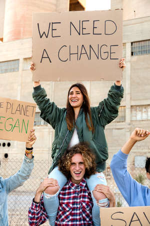 Happy young hispanic woman sitting on mans shoulder protesting against climate change in demonstration. Vertical image.の写真素材