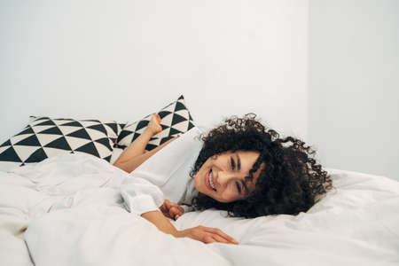 Smiling playful mixed race woman lying on bed looking at camera. Copy space.の写真素材