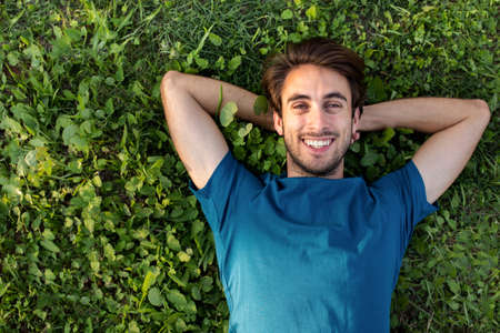 Top view of happy smiling young man relaxing lying on grass looking at camera. Copy space.の写真素材