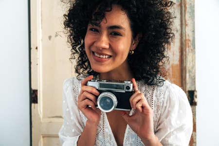 Young smiling multiracial woman looking at camera holds a vintage retro style analog camera.の写真素材