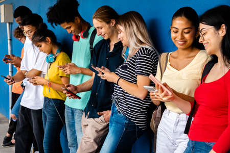 Happy and smiling group of multiracial high school students using cellphone standing against blue wall. Social media.の写真素材