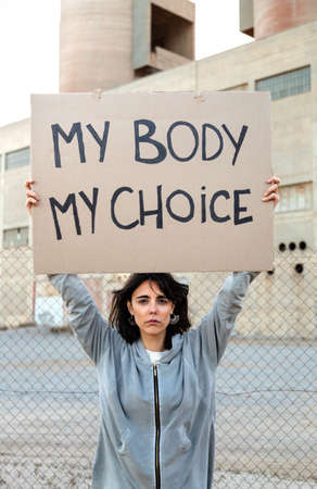 Vertical portrait of young caucasian woman looking at camera holding cardboard sign: My body my choice.の写真素材