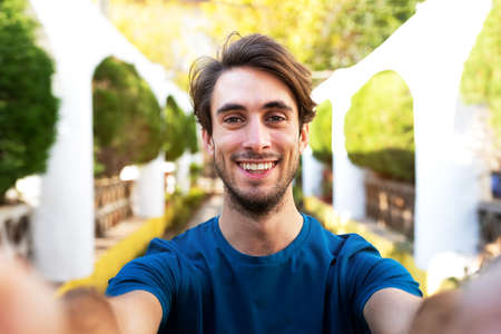 Front view of young man taking selfie holding the camera outdoors in city park.の写真素材