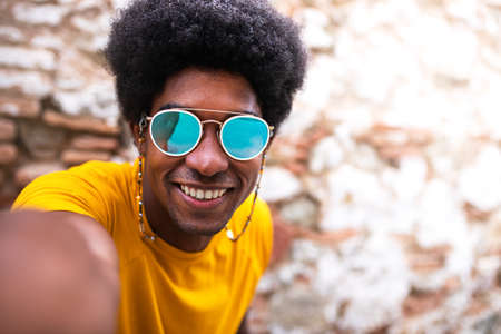 Happy, smiling young African American man taking selfie looking at camera. Copy space. Brick wall background.の写真素材