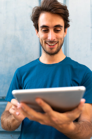 Vertical portrait of happy smiling young caucasian man using digital tablet outdoors. Selective focus on face.の写真素材