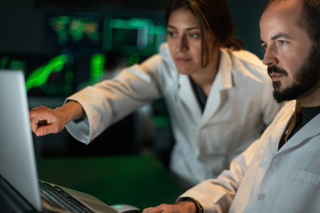 Female scientist shows male doctor colleague some experiment results in the laptop. Working in...