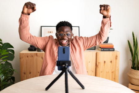 African American black male influencer live streaming with cellphone celebrating success with his followers.の写真素材