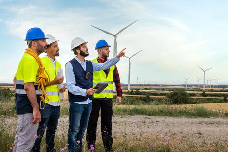 Electric engineer, pointing at windmill turbine farm, explaining maintenance workers maintenance plans. Renewable energyの写真素材