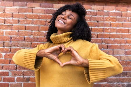 Happy, smiling young African American woman making heart shape with hands in front of chest.の写真素材