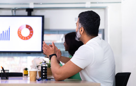 Young indian man applauding during business meeting celebrating great company sales with coworkers.の写真素材