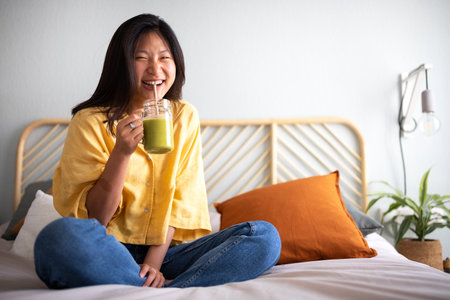 Happy young asian woman laughing. Female Chinese teenager looking at camera drinking green juice smiling. Copy space.の写真素材