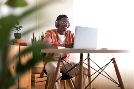 Long shot of young African American man wearing headphones working, studying at home using laptop. Copy space.の写真素材