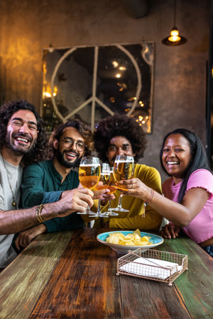 Happy multiracial friends in a bar looking at camera toasting with beer. Vertical imageの写真素材