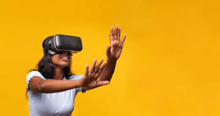 Young indian woman wearing virtual reality simulator gesturing on yellow background. Horizontal banner.の写真素材