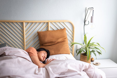 Teen Asian female lying down in cozy bed sleeping at home big bright bedroom. Lifestyle.