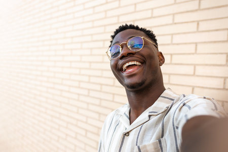 Happy, smiling young African American man with glasses taking selfie. Copy space. Brick wall background.の写真素材