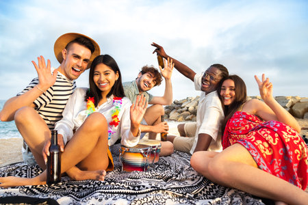 Happy, smiling group of multiracial having fun at the beach drinking beer together waving hand at camera.の写真素材