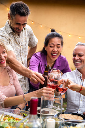 Vertical portrait of asian young woman toasting with wine, celebrating with friends, laughing. Garden dinner party.の写真素材
