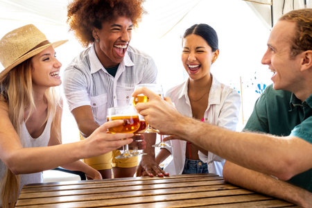 Young black man and his multiracial friends toasting with beer at a beach bar during summer...