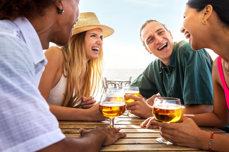 Group of multiracial young friends laughing having fun at beach bar drinking beers together. Friends on summer vacation.の写真素材