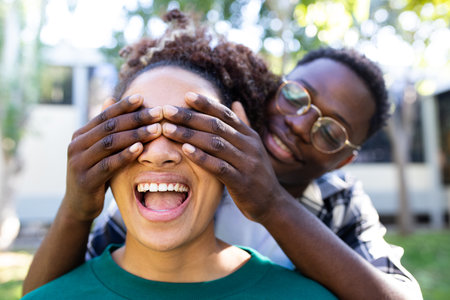 Young African American man covering eyes of surprised girlfriend. Focus on girl face.の写真素材