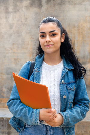 Vertical portrait of female caucasian college student looking at camera carrying folders and a backpack.の写真素材