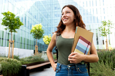 Pensive young redhead university female student looking away standing outdoors in college campus....