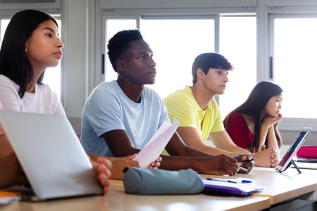 Black teen high school student in class listening to lecture with multiracial classmates. Focus on african american boy.の写真素材
