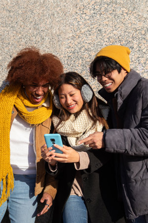 Happy multiethnic university student friends having fun using mobile phone together during sunny winter day. Verticalの写真素材