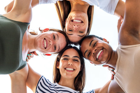 Low angle view of multiracial girl friends heads in circle. College student female friends smiling looking at camera.の写真素材