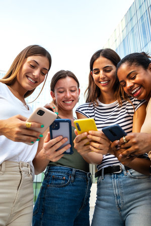 Vertical portrait of happy multiracial group of young women friends looking at mobile phone.の写真素材