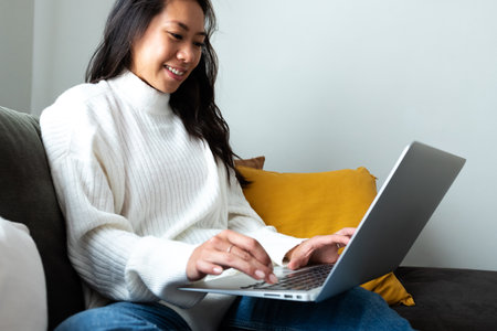 Young Asian woman sitting on the sofa using laptop working at home living room.