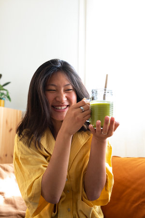 Happy teen asian girl showing healthy green juice. Vertical image.の写真素材