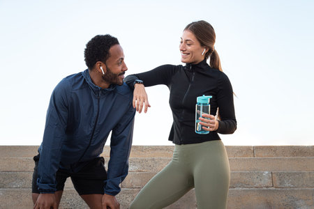 Happy multiracial couple taking a break after running and working out together outdoors.Female holding water bottleの写真素材