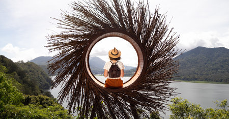 Female traveler contemplating nature sitting in straw nest looking at lake view in Munduk, Bali. Banner image.の写真素材