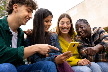 Happy multiracial teen college students having fun using mobile phone together in campus outdoorsの写真素材