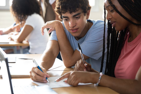 Teen male high school student helping African American female classmate with homework.