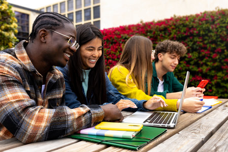 Happy multiracial college students outdoors in college campus studying using laptop.の写真素材