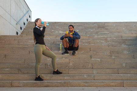 Young multiracial couple taking a break after running together outdoors. Female drinking water. Copy space.の写真素材