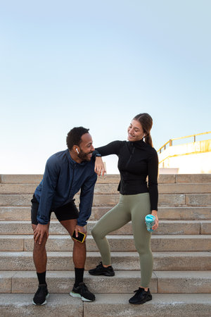 Vertical portrait of tired multiracial couple taking a break after running and working out together outdoors. Copy spaceの写真素材