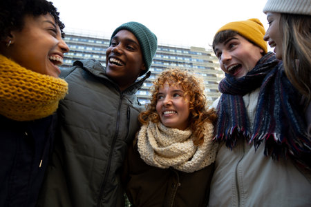 Group of multiracial college friends laughing and having fun embracing together during winter in the city.の写真素材