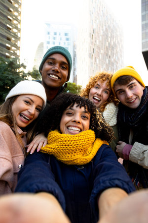 Vertical selfie of african american woman and multiracial group of college friends looking at camera laughing in winter.の写真素材