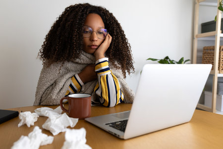 Sick African American woman working from home office using laptopの写真素材