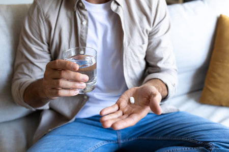 Close up of Caucasian male hand holding pill and glass of water. Man taking medication.の写真素材
